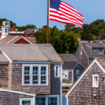 American flag waving above historic Nantucket shingle cottages on a clear day