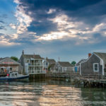 Historic Nantucket wharf with shingle buildings, docked boats, and calm harbor water at sunset