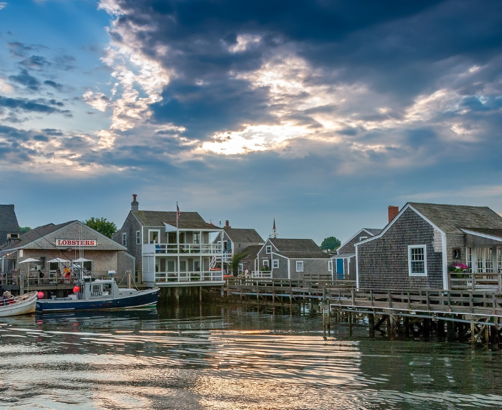 Historic Nantucket wharf with shingle buildings, docked boats, and calm harbor water at sunset